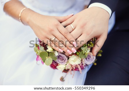 Hands of bride and groom with rings on wedding bouquet. Marriage concept. Royalty-Free Stock Photo #550349296
