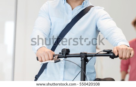 Young businessman holding bicycle with colleague in background at office