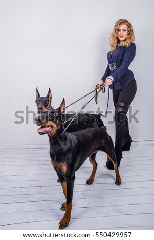 Blonde girl with two Dobermans on a light background