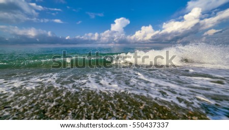 Tilt and shift view of green glowing sunny wave of Black Sea with frozen flying droplets under blue cloudy sky