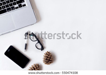 White office desk table with laptop, smartphone, pine cone and glass. Top view with copy space, flat lay.