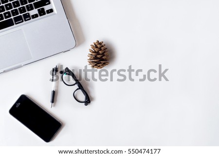 White office desk table with laptop, smartphone, pine cone and glass. Top view with copy space, flat lay.