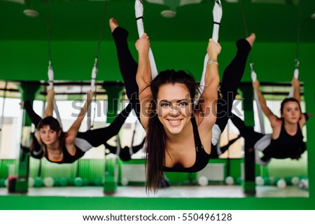 young women making antigravity yoga exercises with a group of people. aero fly fitness trainer workout. white hammocks, eco green background studio. interior mirrors