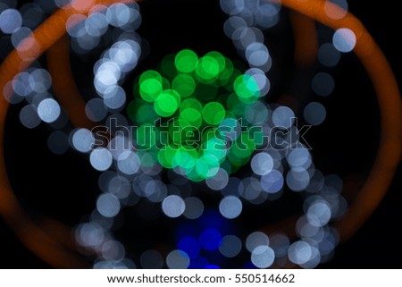 Illumination in the night city - a colorful pattern of blurry lights with greenery spot in the center.
