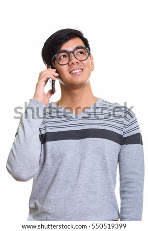 Thoughtful happy Asian man smiling while talking on mobile phone isolated against white background