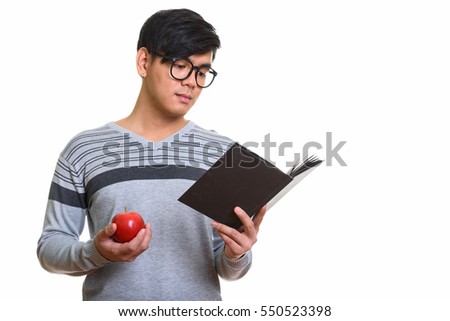 Studio shot of handsome Asian man reading book while holding red apple isolated against white background