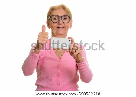 Happy senior nerd woman smiling while taking picture with mobile phone and giving thumb up isolated against white background
