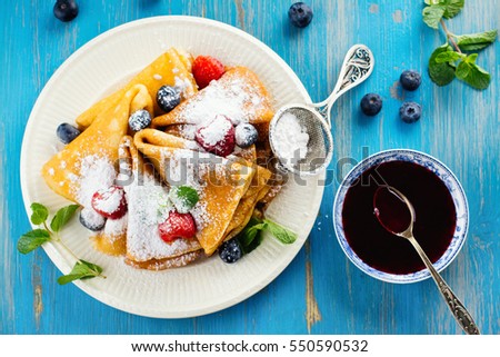 Crepes with jam, berries and sugar powder. Homemade pancakes, delicious breakfast