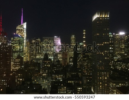 Night skyline photo midtown Manhattan, New York City high above cityscape rooftop view. Dark sky lights illuminate outside big apple exterior
