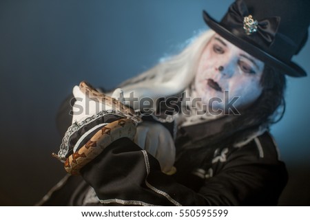 Thick actor in makeup in masquerade dress holding a snake.