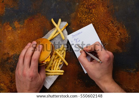 Man making to do list for tomorrow and eating unhealthy fast food today. Procrastination concept.  Top view. Selective focus Royalty-Free Stock Photo #550602148