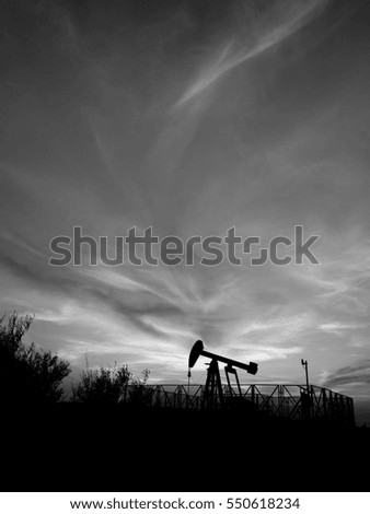 Silhouette of crude oil pump at sunset blue hour in the oilfield- black and white 
