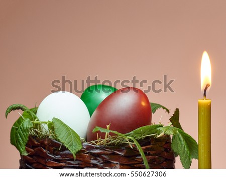Burning candle next to the Easter basket with colored eggs