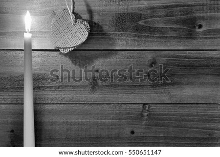 Burning Candle with Burlap Heart on Wood Background - Photograph of a burning taper candle next to burlap heart against a wood background, with a filter on the image for effect.  Blank space for text.