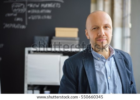 Friendly thoughtful business manager standing in the office looking intently at the camera with a quiet smile, with copy space