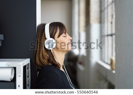 Businesswoman relaxing listening to music on stereo headphones during her lunch break with eyes closed and a blissful smile Royalty-Free Stock Photo #550660546