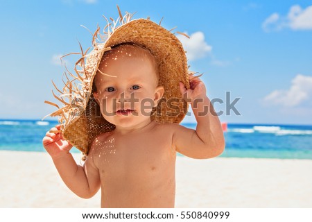 Funny photo of happy baby boy on beach with straw hat and dirty face covered with sand. Family travel, healthy lifestyle, recreation, water outdoor activity on summer beach vacation with children.