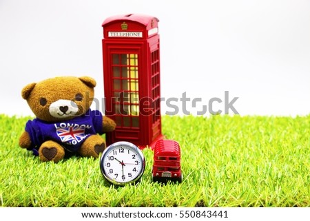 Teddy Bear with clock and red double decker bus and telephone booth are on green grass, Idea of London, England concept.

