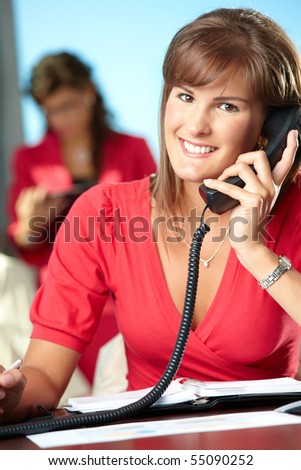 Young businesswoman sitting at desk in office, talking on landline phone, smiling.