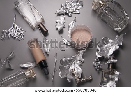 make up still life on the gray background cosmetics. make up setup is decorated with silver leaves includes perfume bottles, skincare products, powder, blush, beauty trends still life