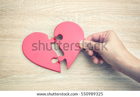 female hand matching red jigsaw heart halves on grey wooden background Royalty-Free Stock Photo #550989325
