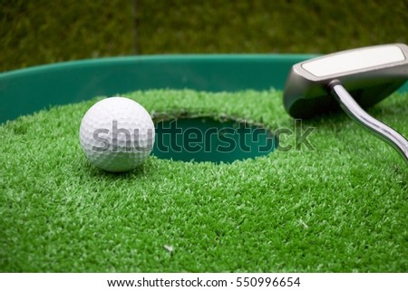 Golf ball and putter are on green grass with clock, idea is time for golf concept.
