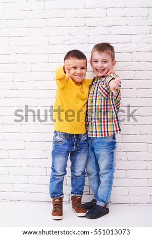 Mid shot of two cheerful peers gesturing with two thumbs down. Standing in front of white wall. Isolated in studio. The concept of friendship 