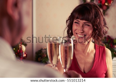 Rack shot of toothy laughing senior woman holding champagne flutes celebrating New Year with husband at home. Spending time together, romantic atmosphere 
