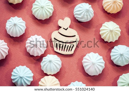  meringues in pastel colors with wooden figure of cupcake on red background