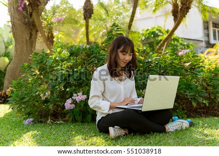 Young woman with laptop sitting on green grass in the park.