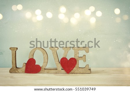 Valentines day background. Word LOVE from wooden letters and red hearts on old table. Glitter overlay