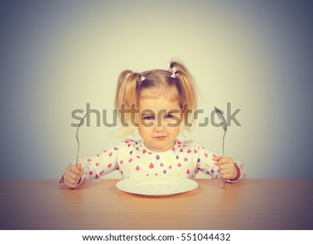 Little girl holding fork and spoon with , empty plate ready for food.