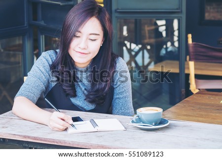 A beautiful asian woman writing on notebook , hot coffee and vintage wooden table background