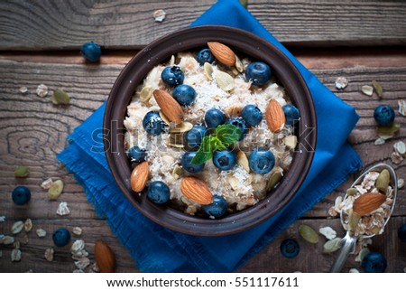 Oatmeal with blueberries, almonds, coconat and seeds at rustic wooden table. Flat lay.
