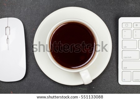 White keyboard, mouse and cup of tea or coffee on blackboard table