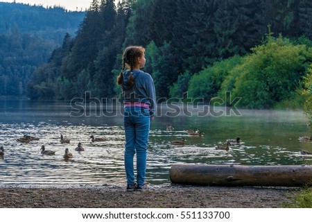 The girl-child near the pond. A child near water. The girl on the background of mountain lake with ducks.