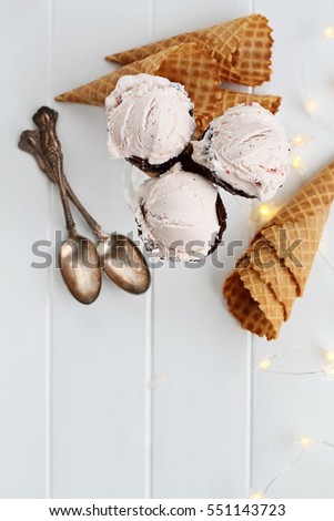 Top view of pink strawberry ice cream gelato in waffle cones shot over a rustic wooden background with fairy lights and antique spoons. Extreme shallow depth of field.