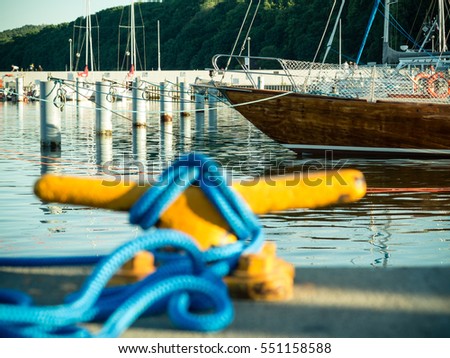 Yellow mooring bollard with blue rope in marina yachts in the background
