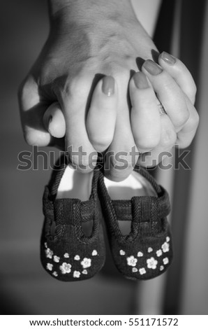 Close picture in black and white of two hands holding together two little baby shoes for an upcoming child. 