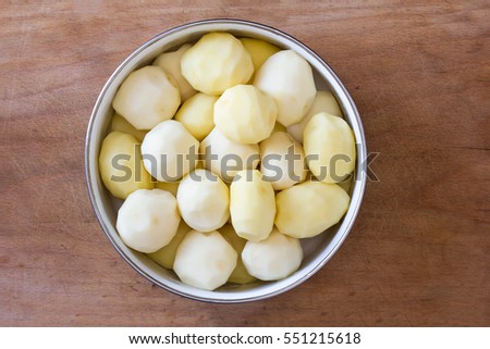 raw peeled potatoes in a circular bowl on an old rustic wooden table closeup, top view.