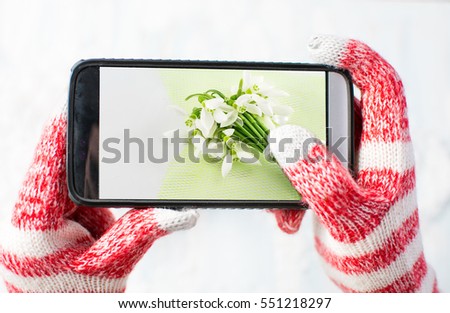 Hands in gloves taking a photo of Snowdrops bouquet