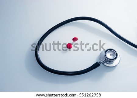 Stethoscope snakes around two red pills that need to be taken urgently upon doctors orders.