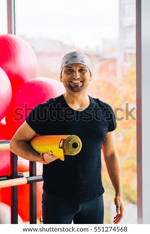 Happy Indian man at the gym holding yoga mat after his practice