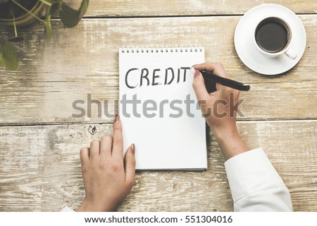 Woman write "Credit" in a notebook with coffee and phone on table