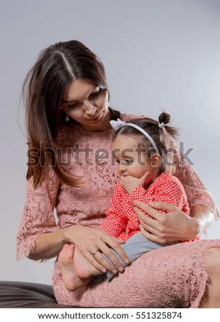 Young mum embraces a daughter on a light background in bright clothes
