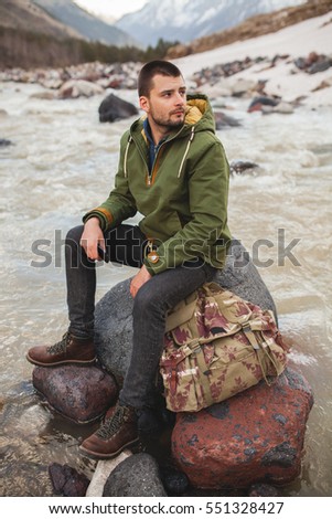 young hipster man, sitting by the river, wild nature, winter vacation, hiking, traveling, backpacker, warm clothes, anorak