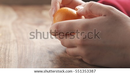 young female hand peels clementine tangerine on wooden table, 4k photo