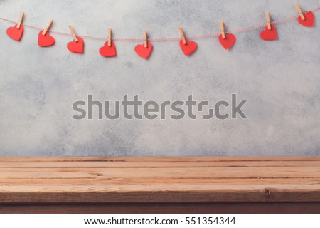 Empty wooden deck table over rustic wall background with heart shape garland. Valentines day concept