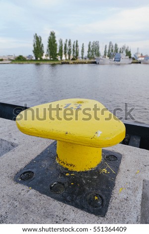 Vertically oriented picture of port pier with yellow mooring bollard.