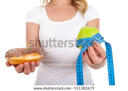 Close up picture of a young woman holding a donut and a green apple in her hands